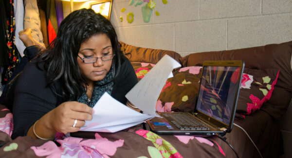 Student lies on bed in residence while studying with laptop