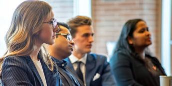 Four students in business attire listening intently in class
