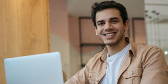 A cheerful man at a table engaged with his laptop, showcasing a moment of productivity and happiness.
