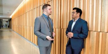 2 students in suits talk in hallway