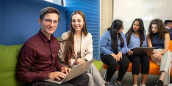 Two students sitting in a common area with male student on laptop and both students looking at the camera smiling. Three students in the background sitting and chatting.