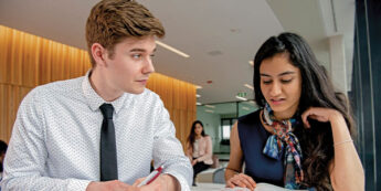 Two students studying together with an open book in a bright, modern workspace.