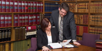 Lawyer looks over page while law clerk student reads through binder of papers