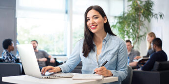 Female student in study room with laptop and pen in hand.