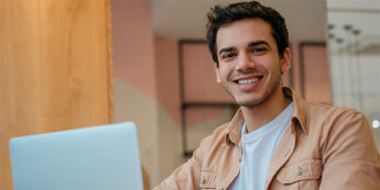 A student at a table engaged with his laptop, showcasing a moment of productivity and happiness.