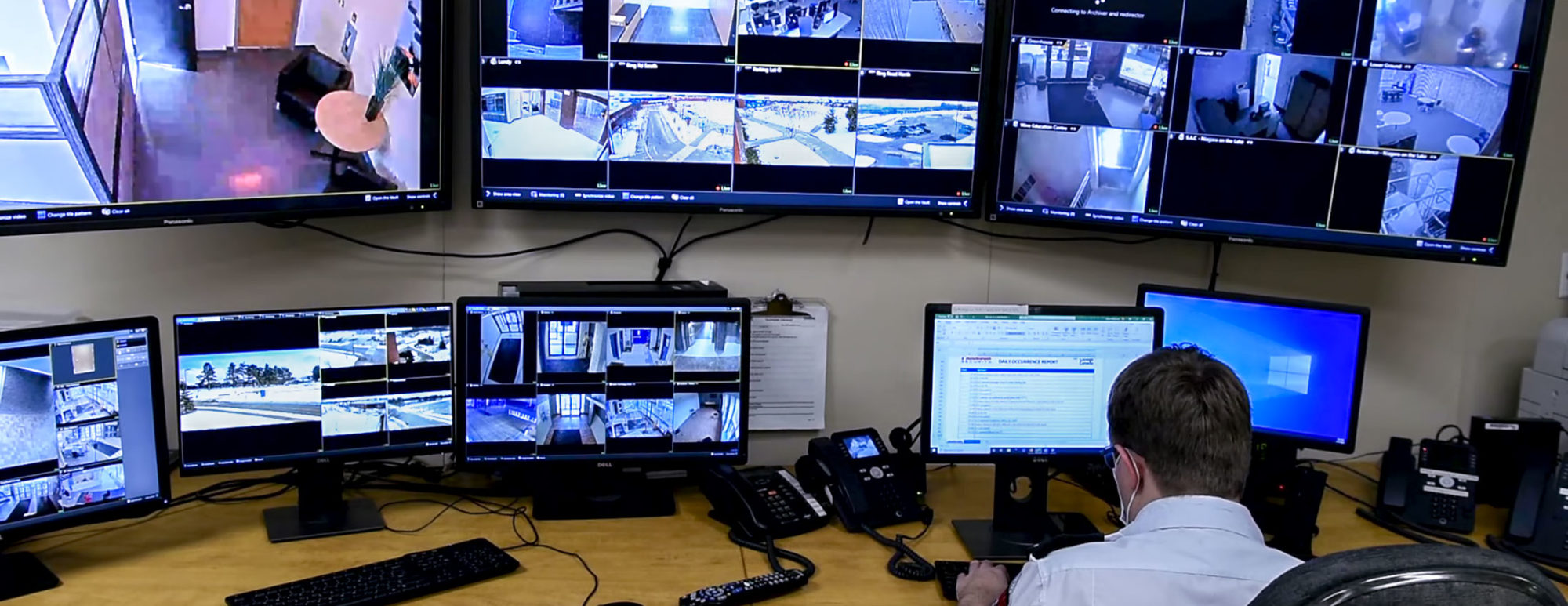 Uniformed security guard sitting in front of CCTV display with many screens