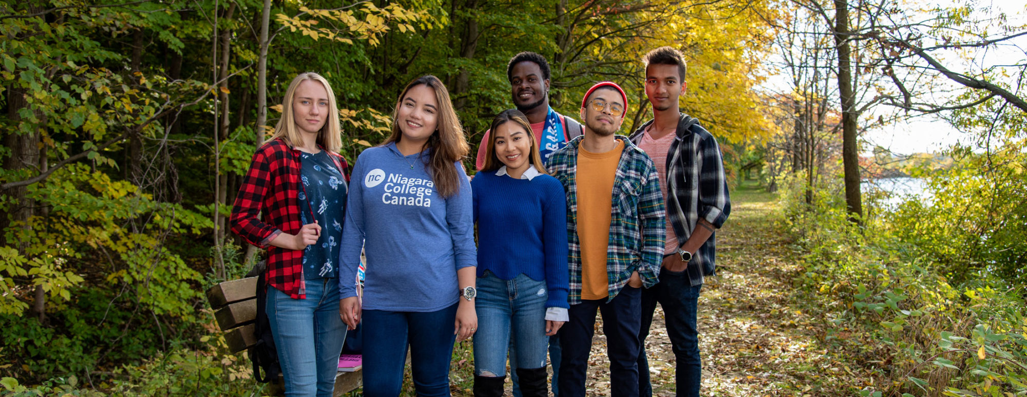 A group of students wearing NC clothing standing outside with colourful fall trees behind