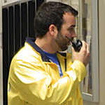 A student wearing a yellow Campus Watch coat talks on a radio
