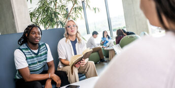 two students sitting on a blue couch in a bright, modern lounge.
