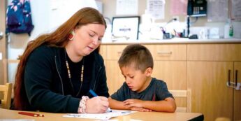 Student working with young child while sitting at a table.