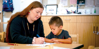 Student working with young child while sitting at a table.