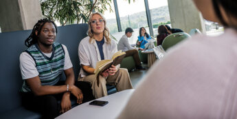 two students sitting on a blue couch in a bright, modern lounge.