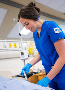 A nursing student practising injecting a needle into a hospital training manikin.