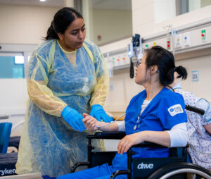Two nursing students, one in a wheelchair practising their skills in the nursing lab.
