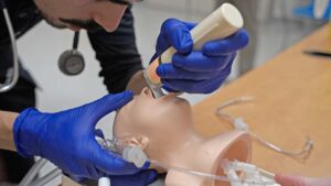 Paramedic student practising intubation on a hospital training manikin.