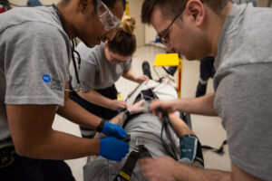 Group of paramedic students practicing skills on another student laying on a gurney in the paramedics lab.