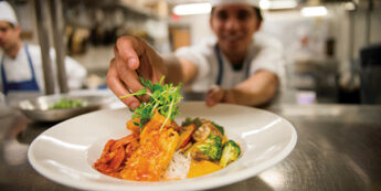 Student serving up salad at the pass of a kitchen.