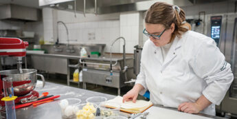 Female student in kitchen reading a recipe from a book in front of her mise en place.