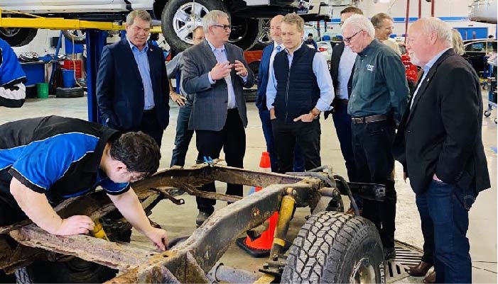 Student working on 0 emmisions vehicle with ministry representatives looking on