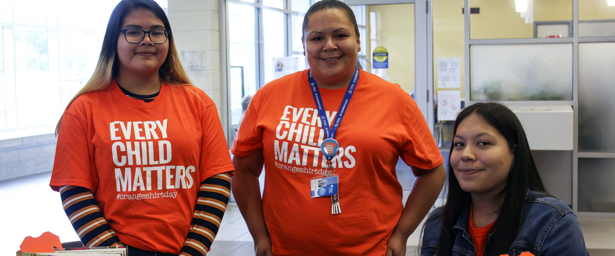 Three students wearing Every Child Matters t-shirts at a booth