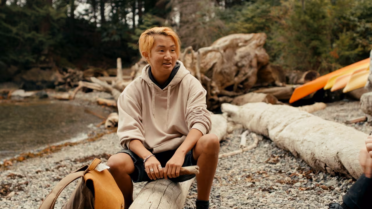 A person sitting on a log by a waterfront.