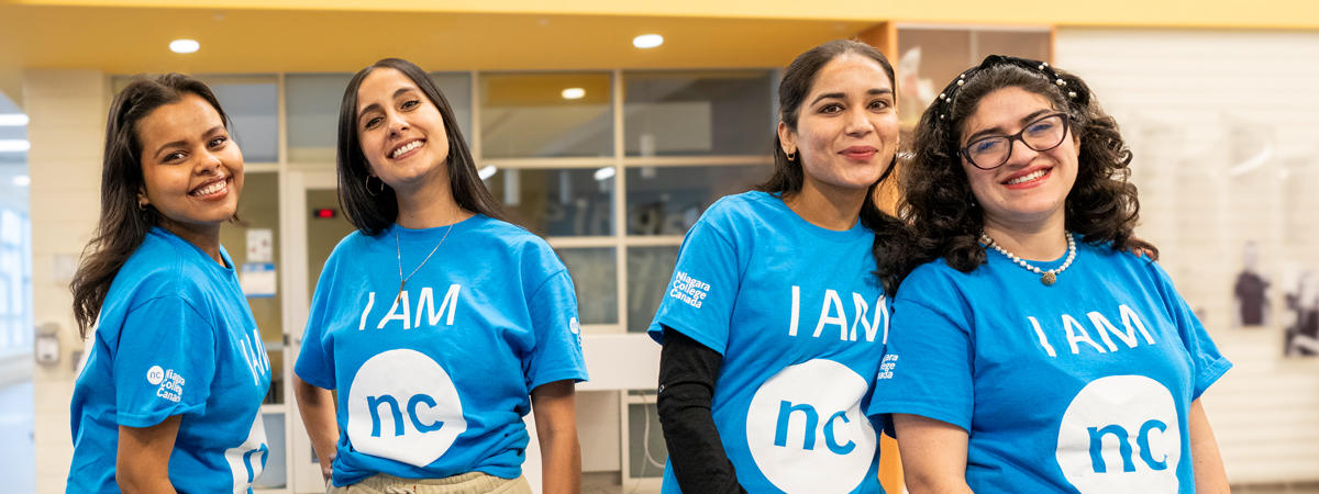 Four female students with I AM NC shirts smiling in a group