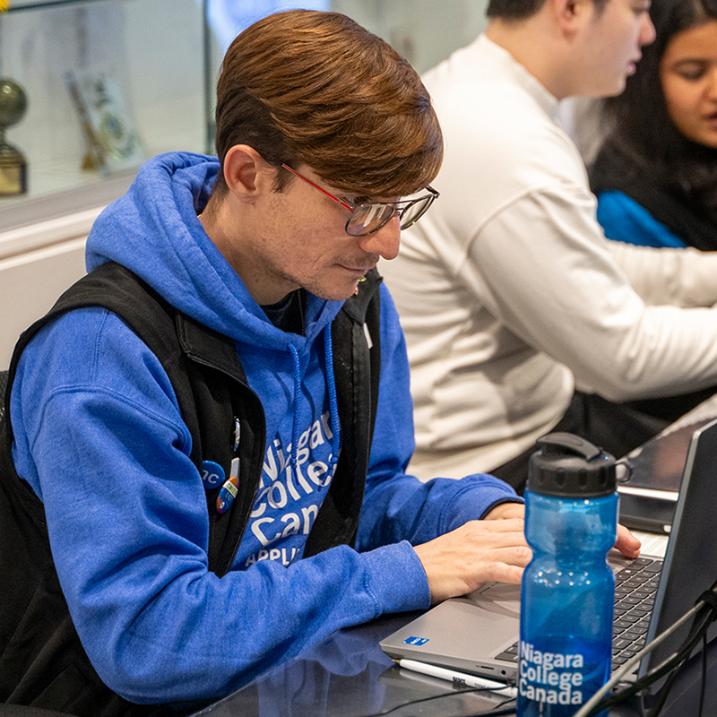 Male student wearing NC attire typing on laptop