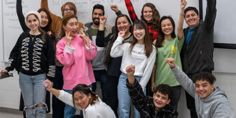 A diverse group of students, poses enthusiastically for a picture in a classroom.