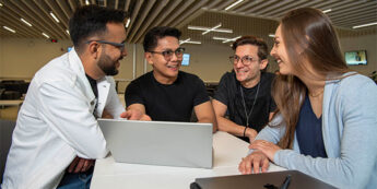 Four young adults are collaborating around a laptop and engaged in conversation.