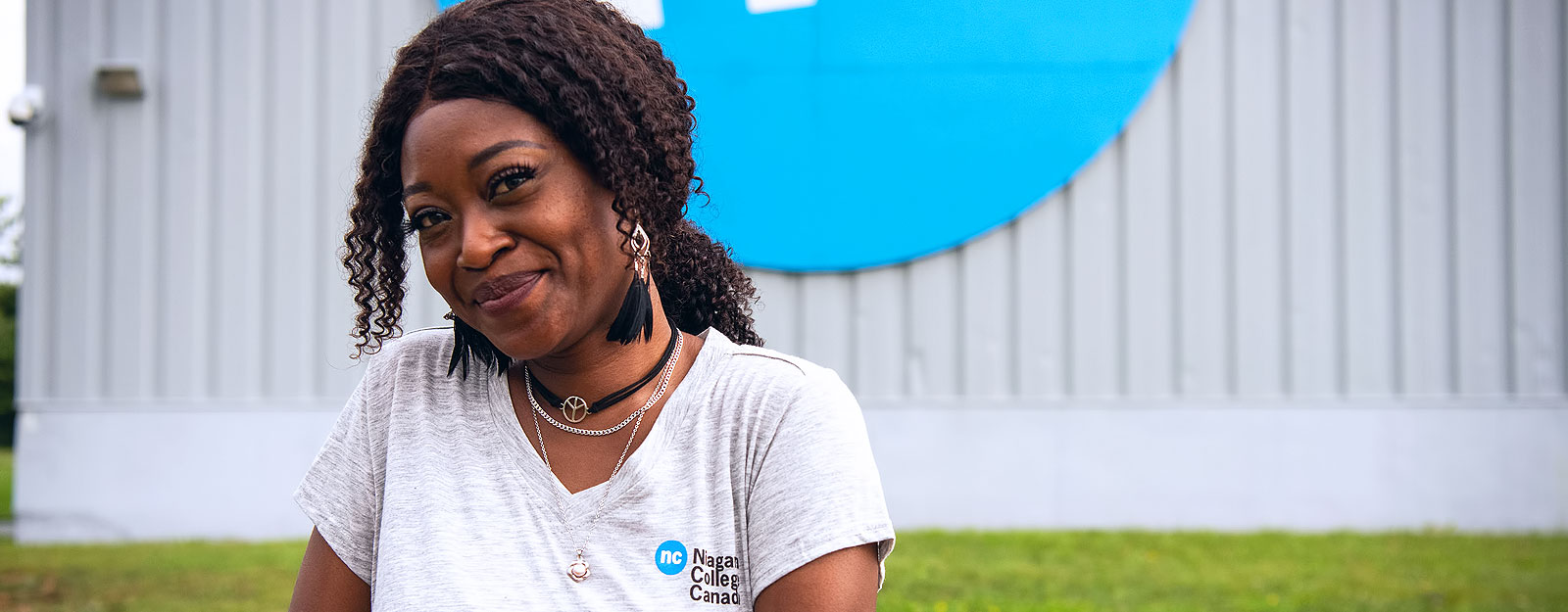 Female student wearing NC t-shirt smiles in front of a large NC logo