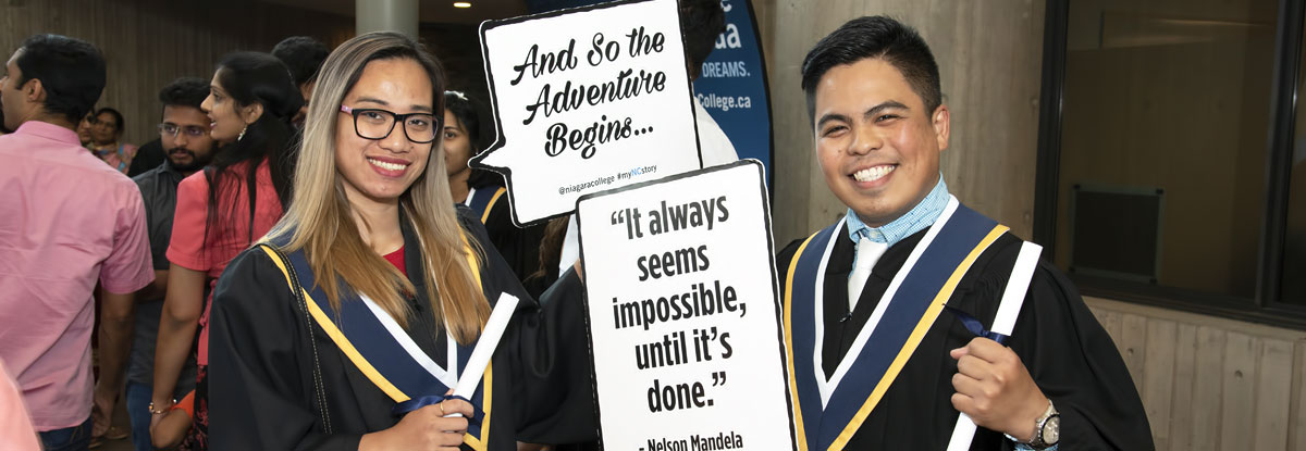 Two graduates holding funny graduation signs