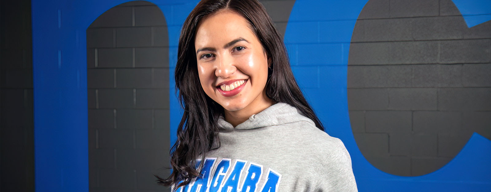 Female student wearing NC sweatshirt standing in front of NC wall