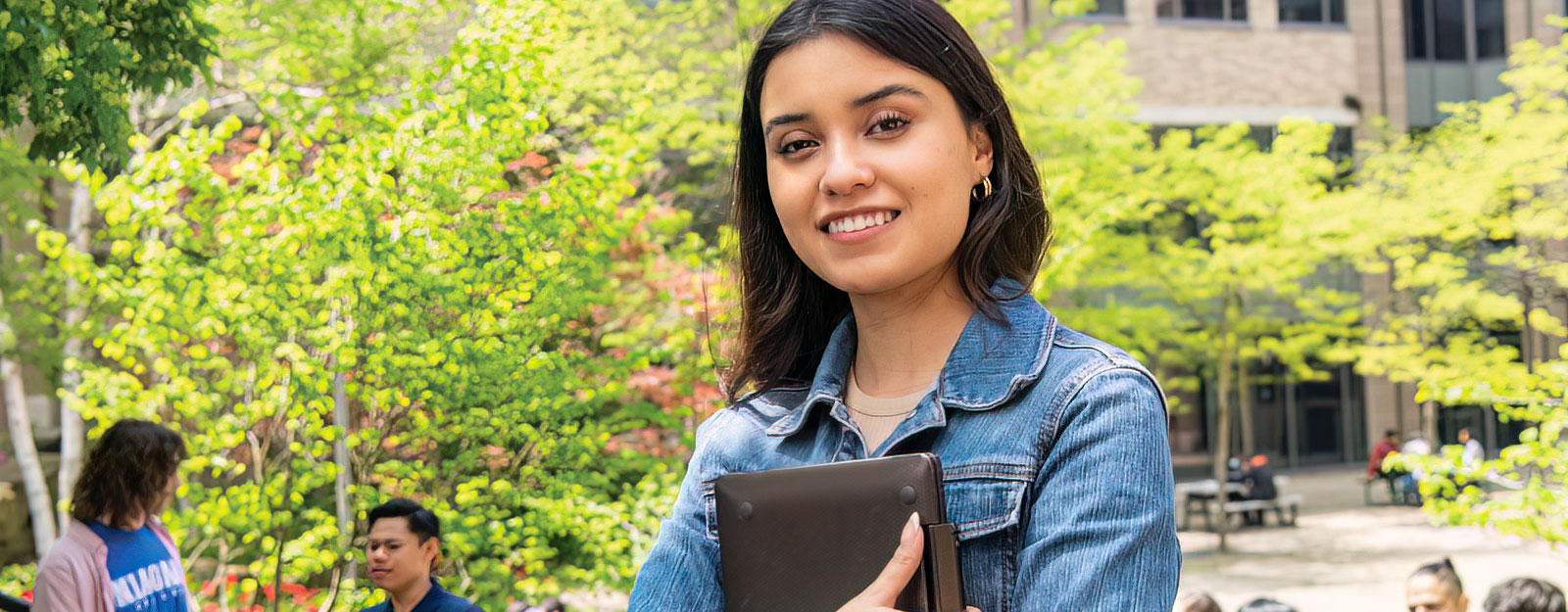 Female student standing outside with leafy tree behind her