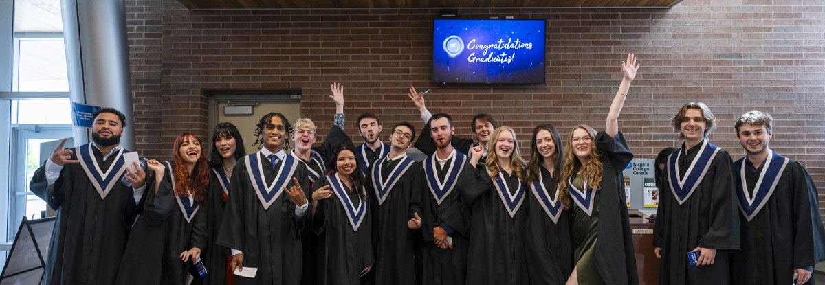 Large group of graduates cheering in front of a Congratulations Graduates sign