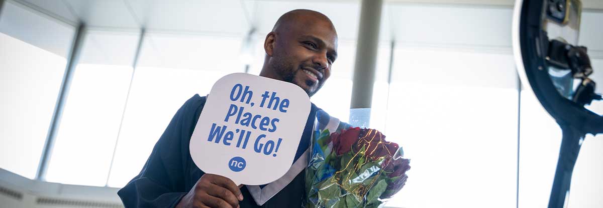 graduate holding graduation sign and flower bouquet