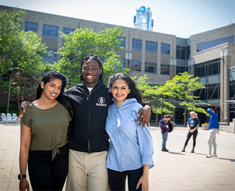 Three students standing together smiling for the camera in front of Niagara College, Niagara on the Lake Campus