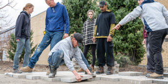 A group of student works together outdoors to lay concrete pavers