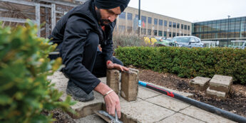 The student is fixing a walkway beside a hedge using tools.