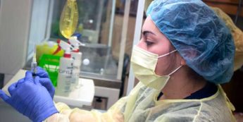 Pharmacy technician in protective gear prepares needle