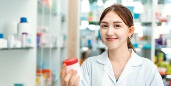 Female pharmacy assistant holding a medicine bottle in a pharmacy.