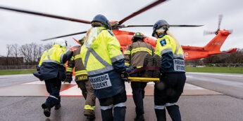 paramedic students carrying a stretcher towards a orange helicopter