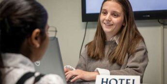 Two students practicing being a hotel reception desk in a classroom.