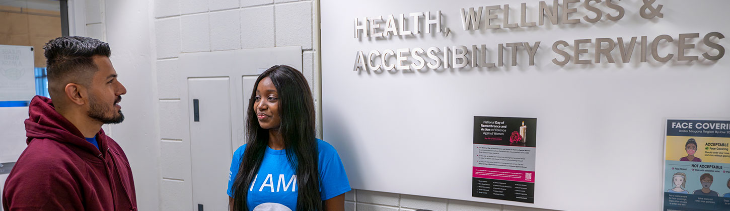 2 students beside the Health, Wellness and Accessibility Services sign.