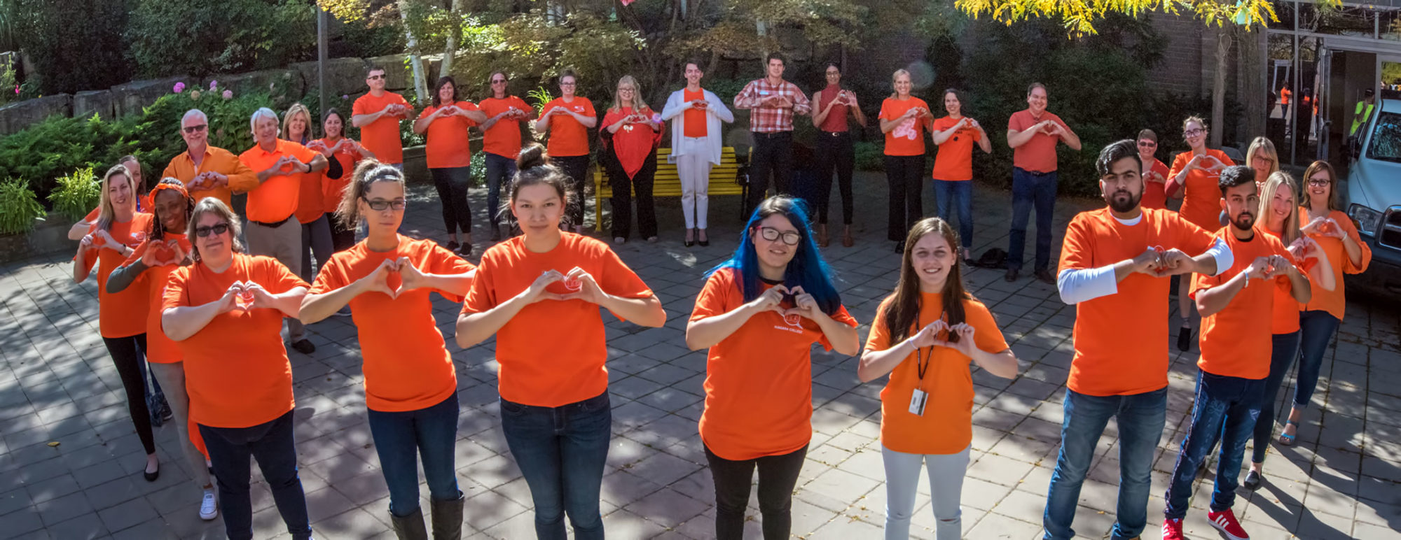 Students wearing orange shirts standing in a circle making a heart gesture with their hands