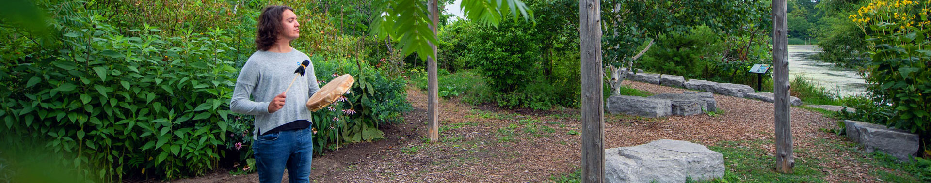 Indigenous student with drum standing in Indigenous garden