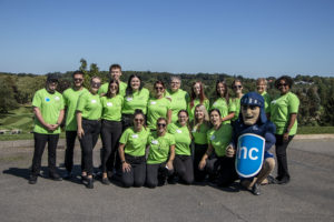 A group of people wearing bright green t-shirts standing with a mascot outside.
