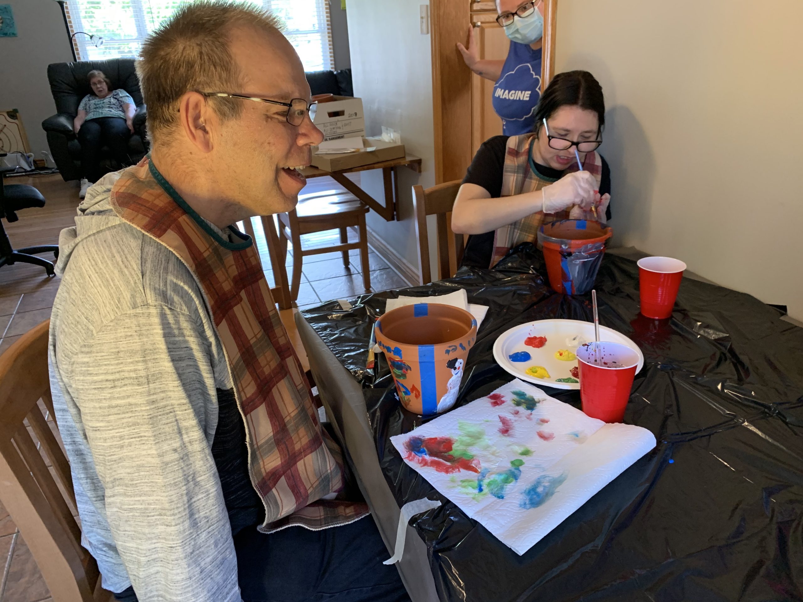 Residents at a Bethesda group home are seated at a table, happily painting plant pots.