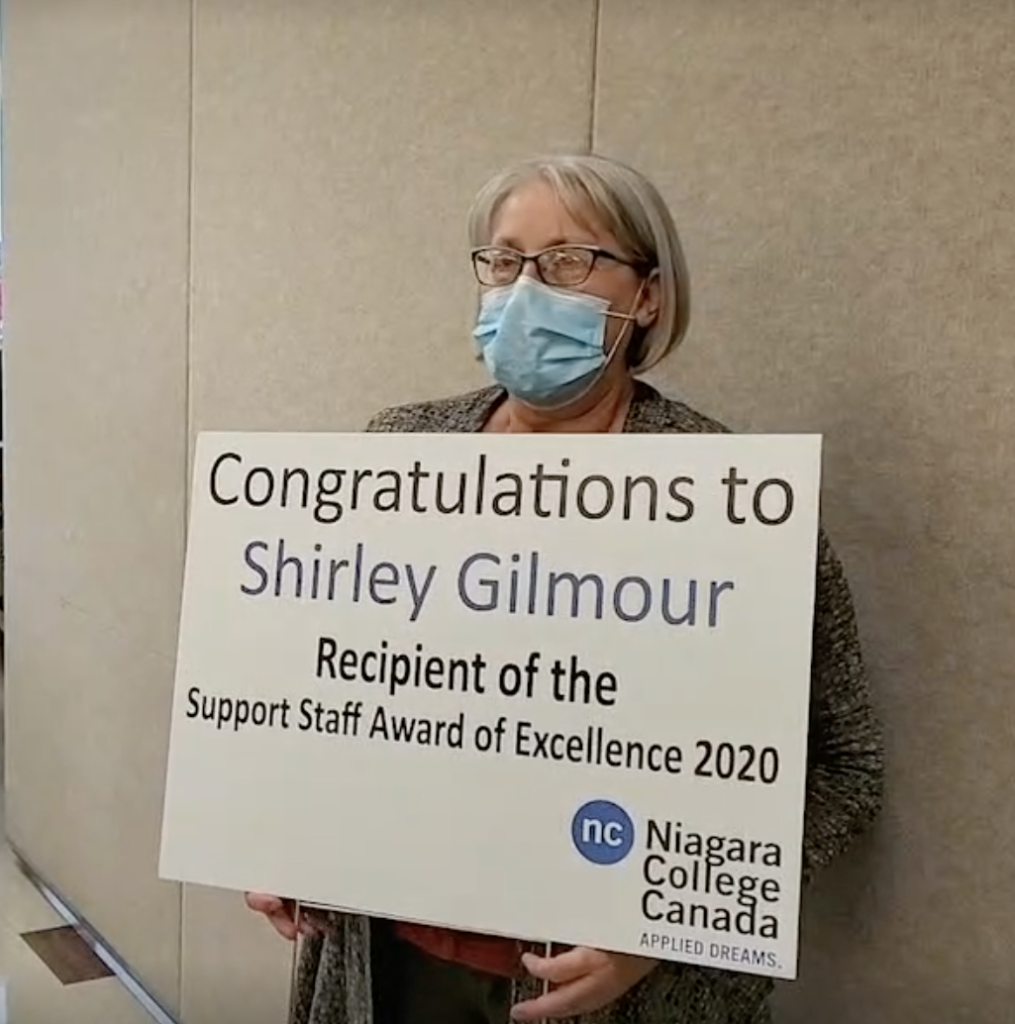 Shirley Gilmour holds a sign congratulating her for winning this year's award of excellence