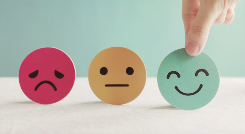 A sad face, indifferent face and happy face emoji wtih a human hand reaching for the happy face
