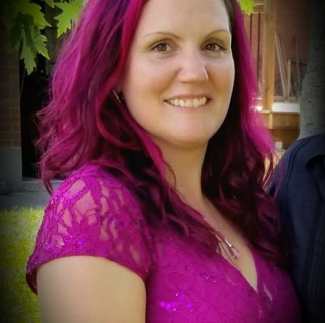 A woman with magenta hair and wearing a magenta shirt smiles into the camera